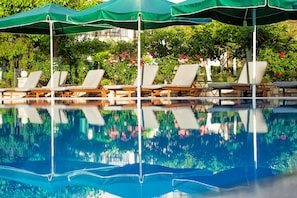 A poolside area with lounge chairs and umbrellas, surrounded by lush greenery and flowers. - Europa Hotel (Archaia Olympia)