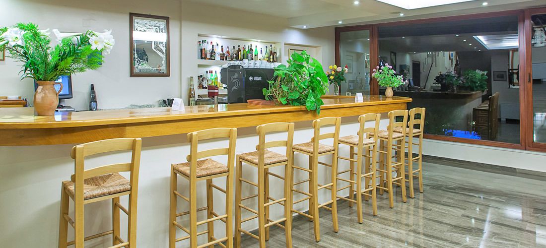 Una zona de bar con sillas de madera y mostrador, una máquina de café y plantas en macetas.