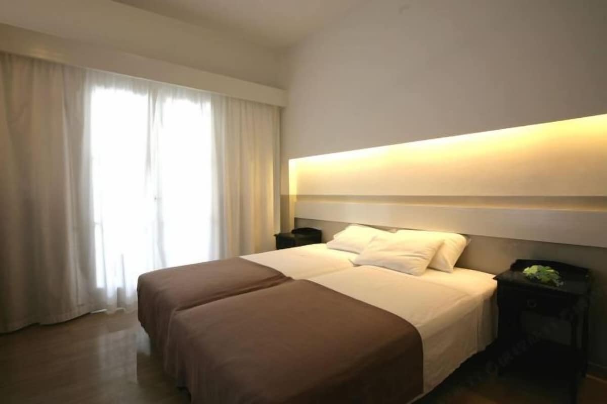 A hotel room with a large bed, a bedside table, and a window with curtains.