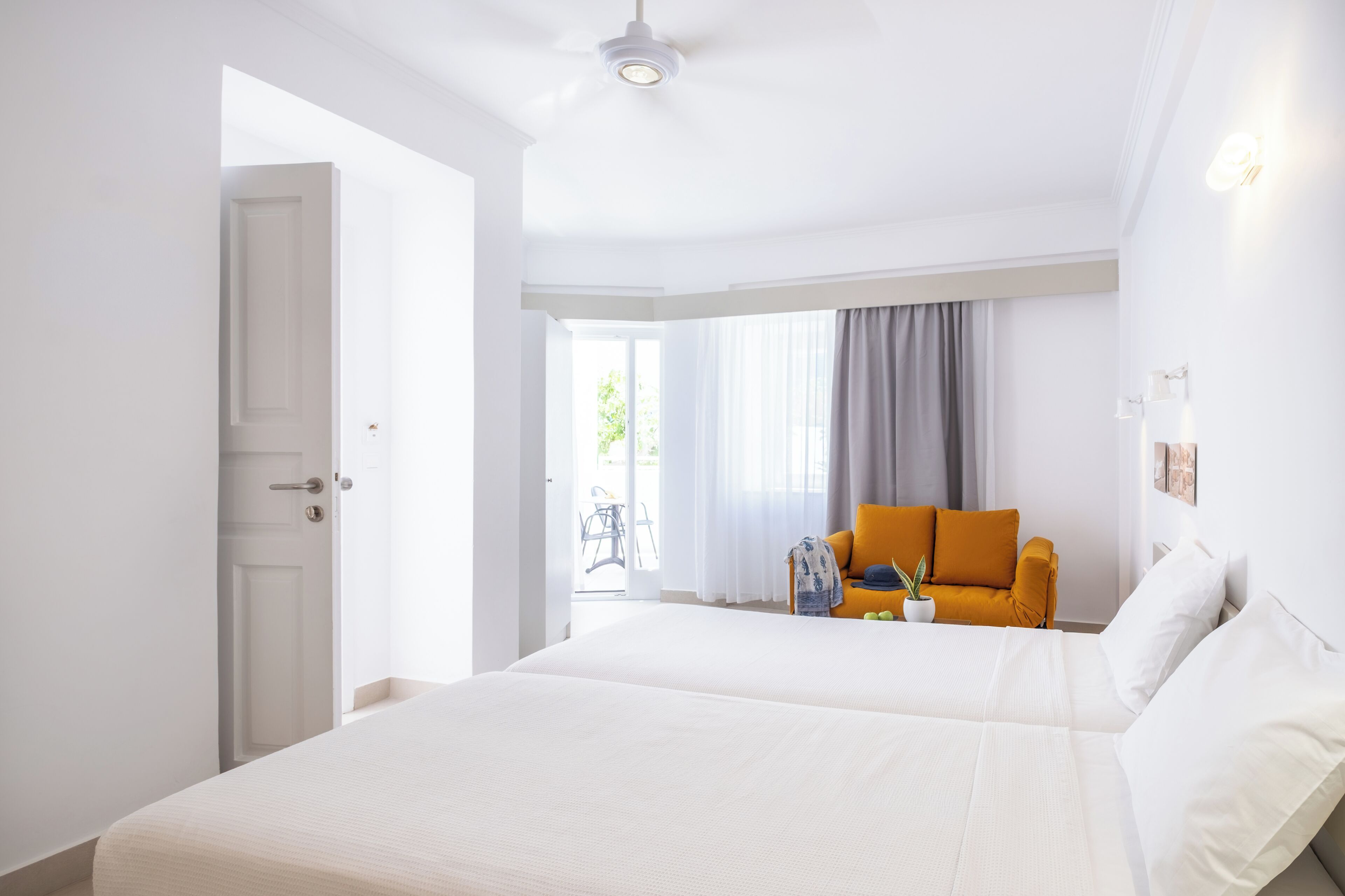 A hotel room with two beds, a sofa, a window with curtains, and a door leading outside.