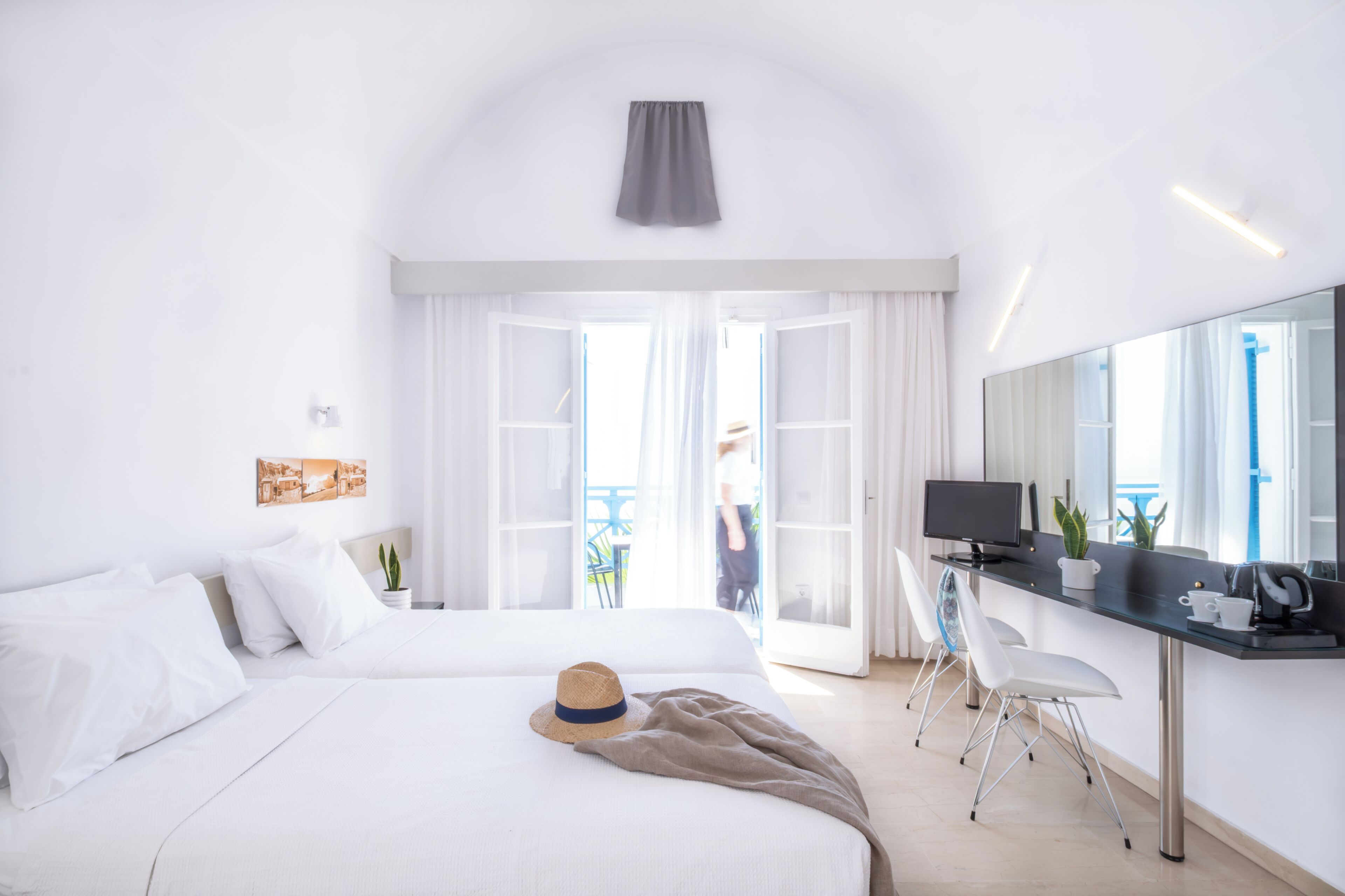 A modern hotel room with a bed, a desk with a computer, a chair, and a balcony with a view.