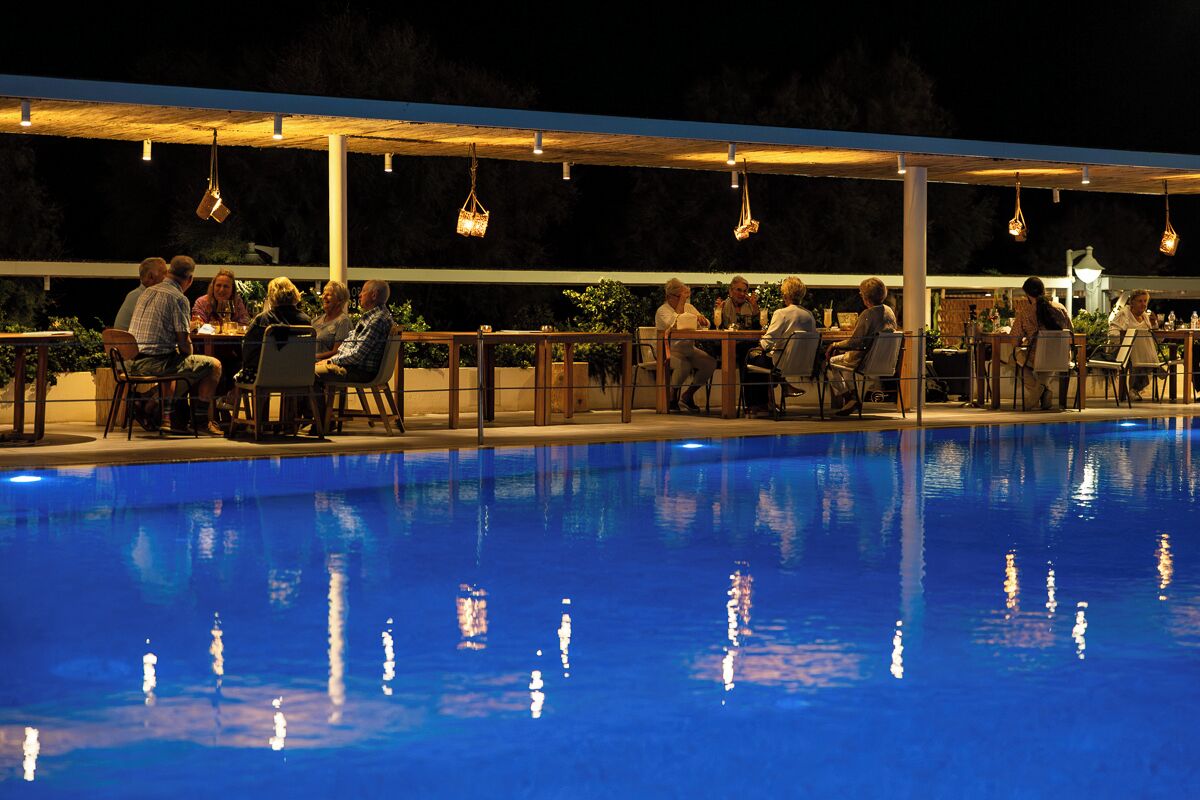 An outdoor pool area with people dining under a covered patio.