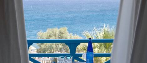 A balcony with a view of the sea, a table with glasses and a bottle, and a blue railing.