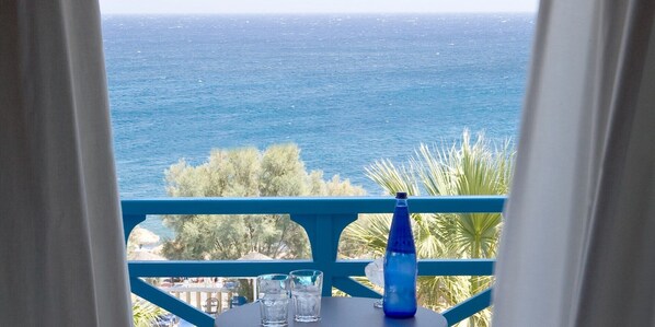 A balcony with a view of the sea, a table with glasses and a bottle, and a blue railing. - Kamari Beach Hotel (Santorini)