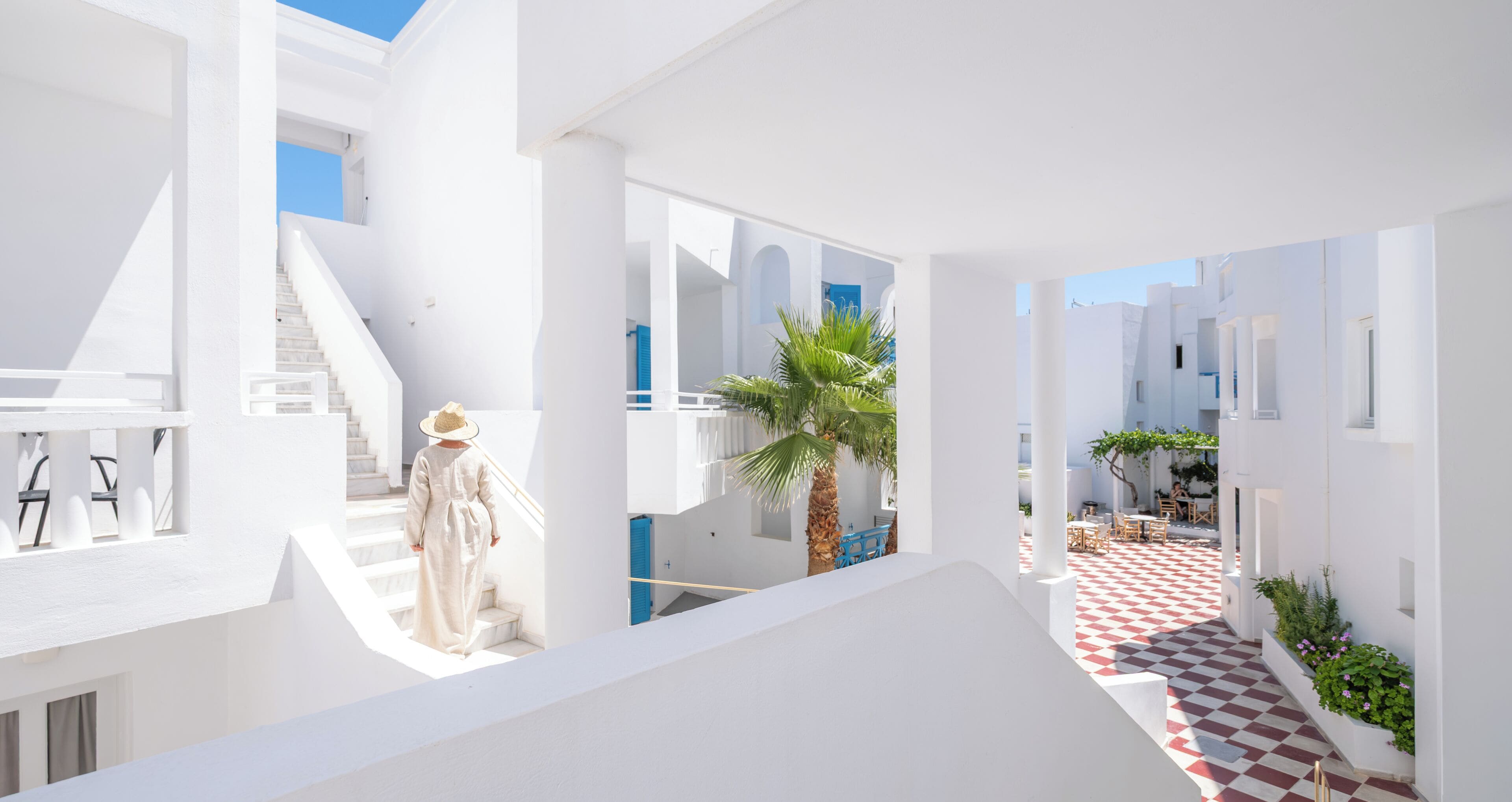 Um edifício moderno branco com uma escadaria, uma palmeira e um piso xadrez.