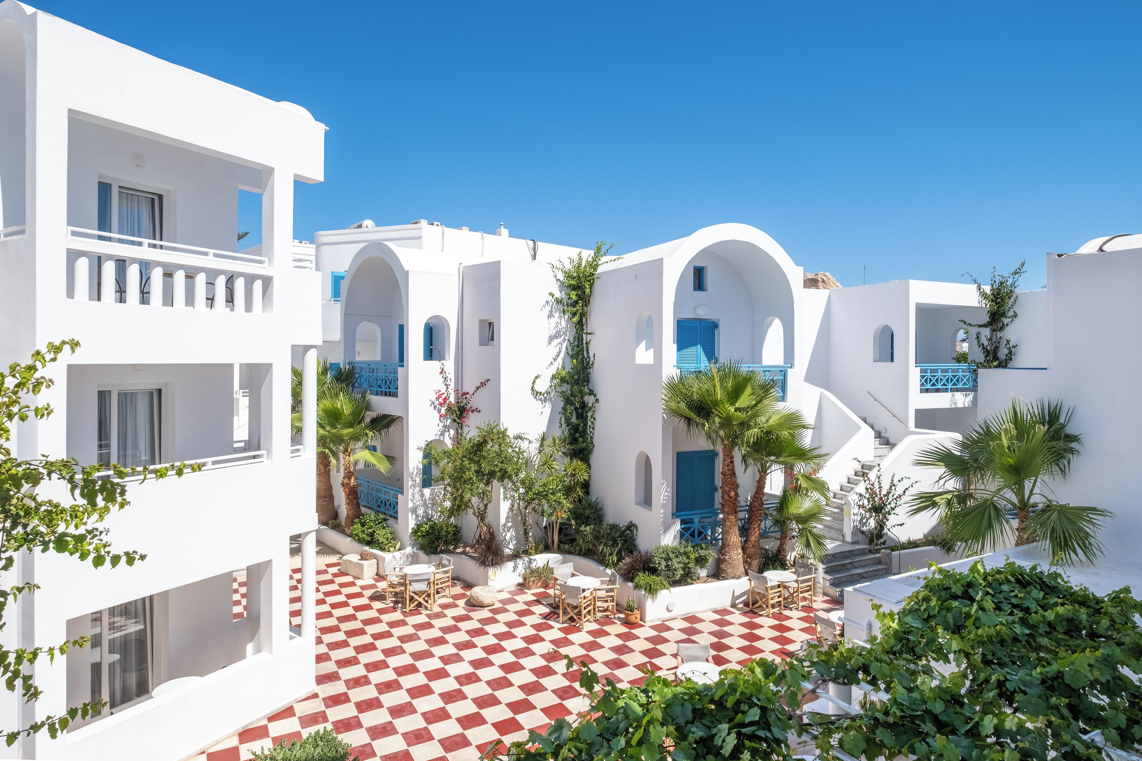 A white building with blue accents, a red and white checkered courtyard, and palm trees.
