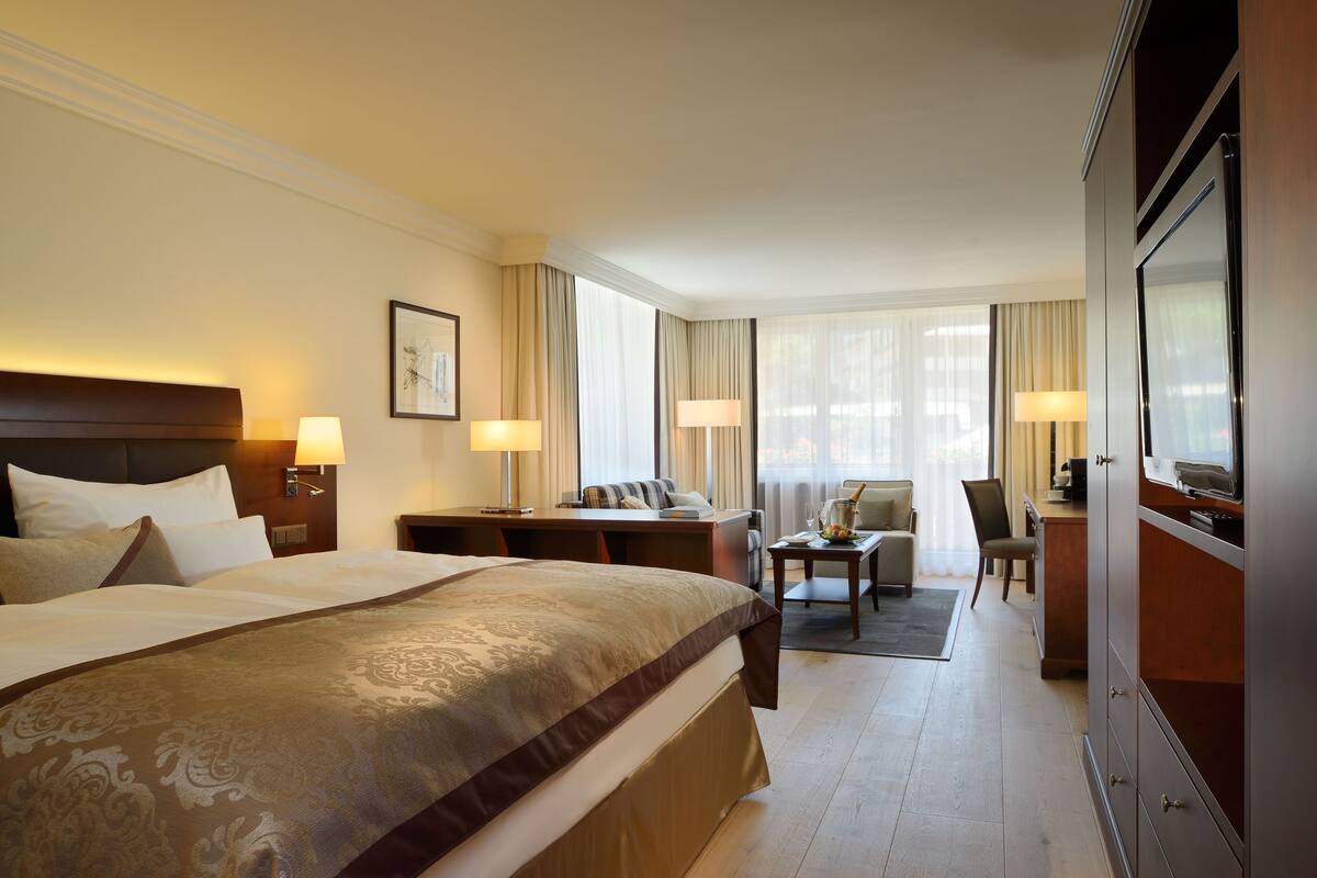 A hotel room with a large bed, a desk, a chair, and a television.