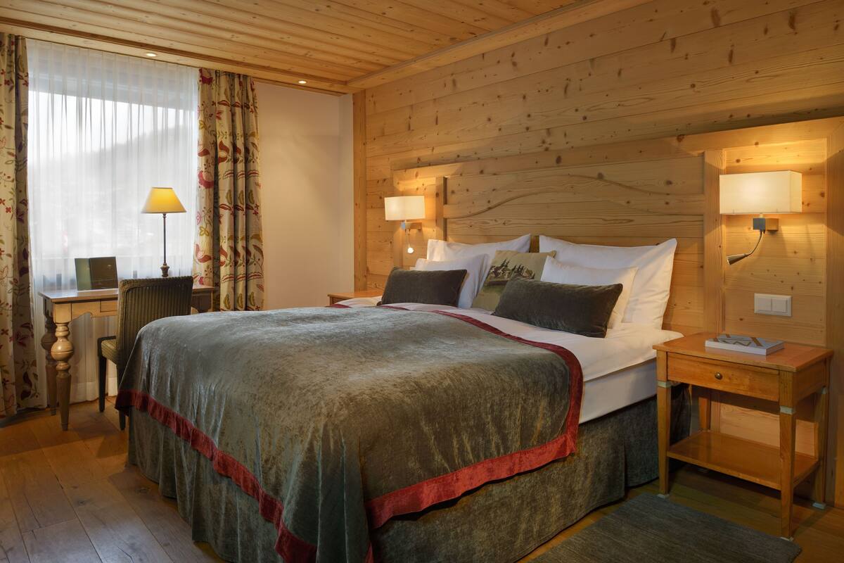 A wooden-paneled bedroom with a large bed, two bedside tables, a desk, and a chair.