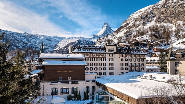 A snow-covered mountain town with a prominent hotel named "Mont-Turin Palace" featuring a swimming pool, traditional architecture, and a view of a snow-capped mountain. - Mont Cervin Palace (Zermatt)