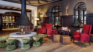 A spacious lobby with a central fire feature, red upholstered chairs, and a bar area. - Mont Cervin Palace (Zermatt)
