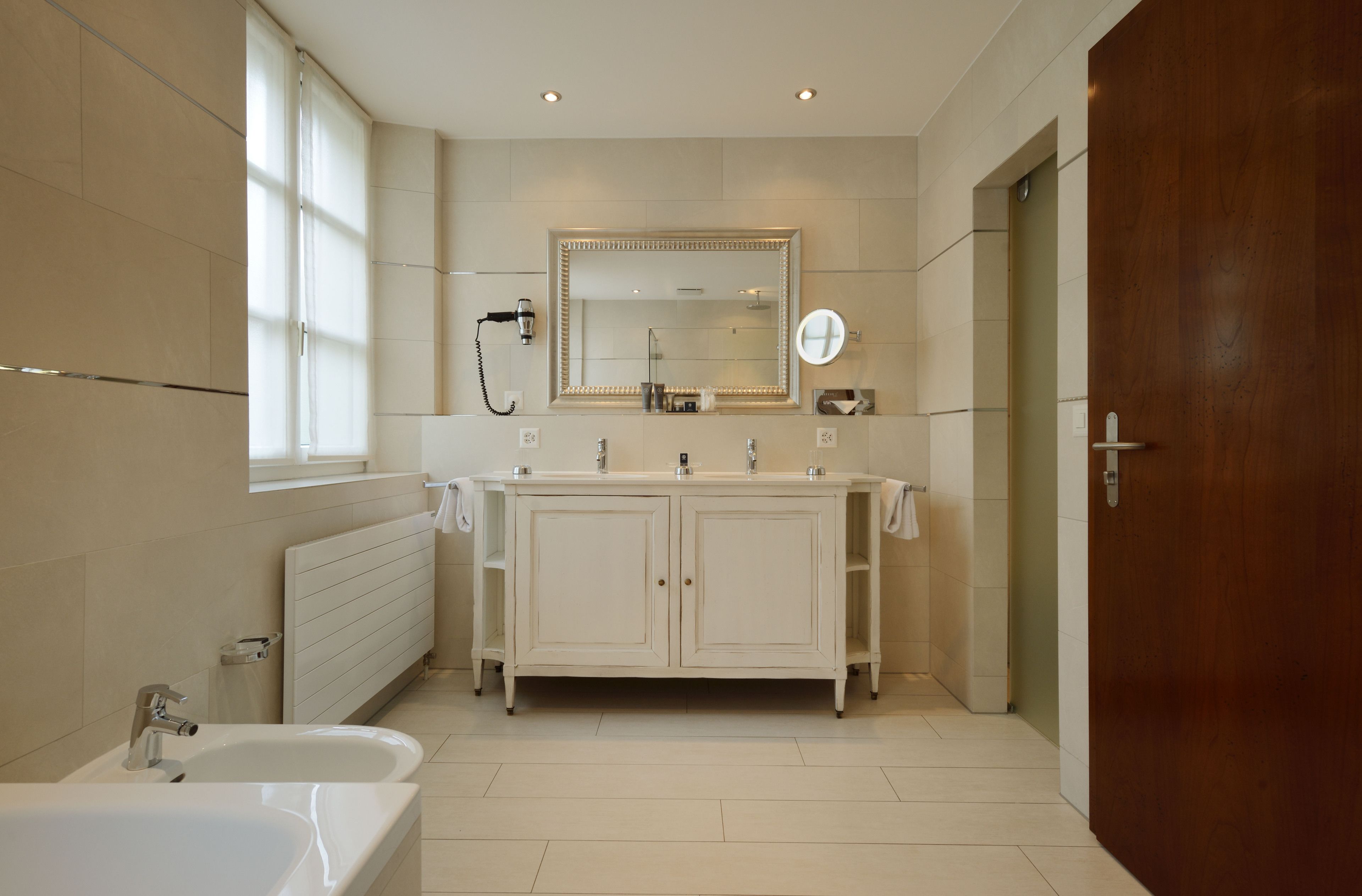 A modern bathroom with a double vanity, a large mirror, and a standalone bathtub.