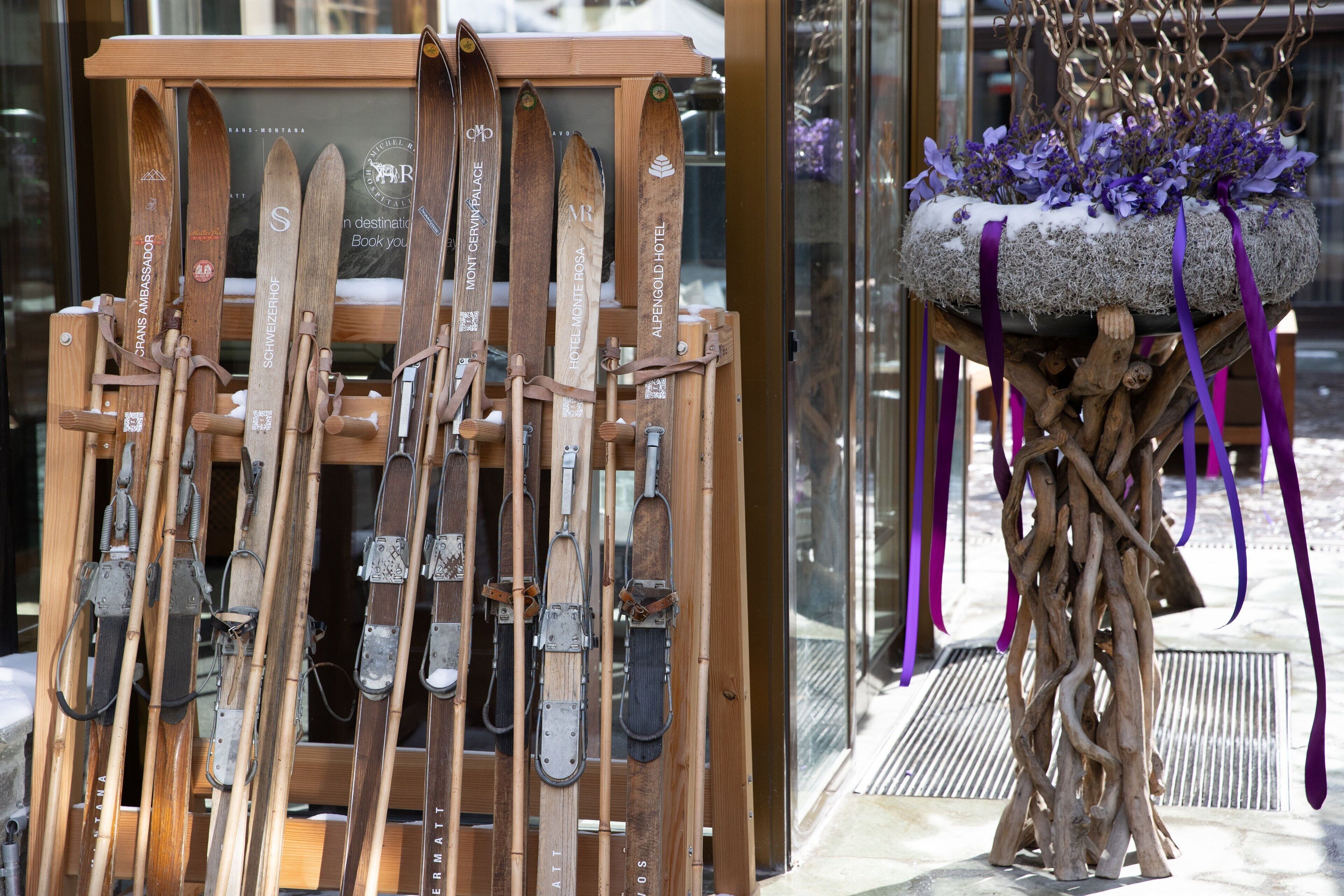 Una rastrelliera in legno per sci con sci e una pianta decorativa con fiori viola.