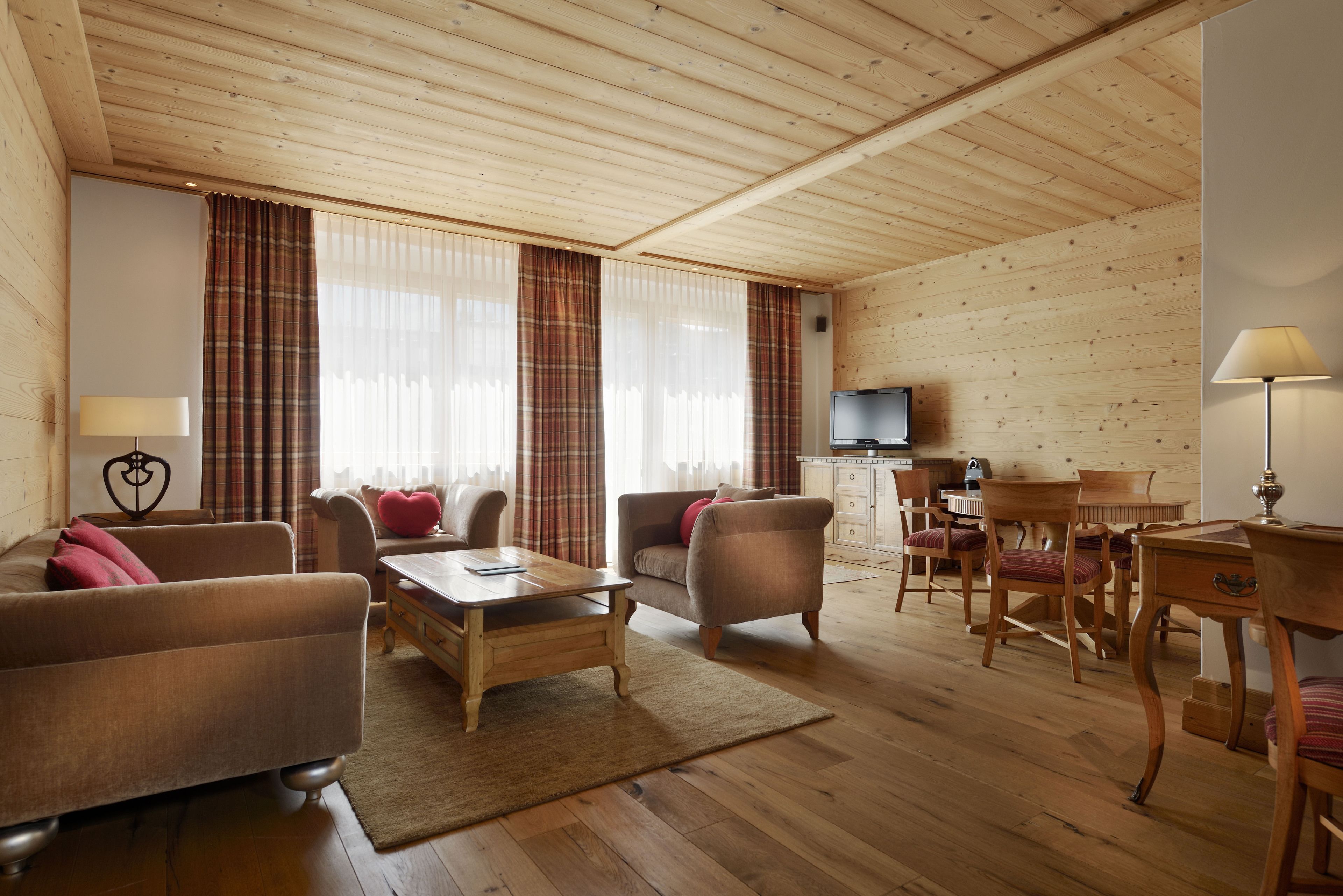 A cozy living room with wooden flooring, a sofa, armchairs, a coffee table, and a television.