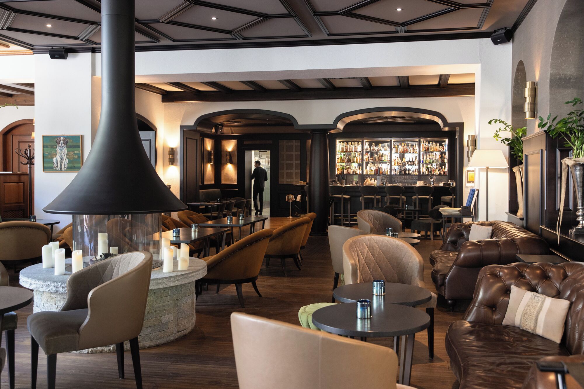Un espace bar proposant différents types de sièges, notamment des tables et des canapés, ainsi qu’une grande lampe noire et un comptoir bien garni de bouteilles.