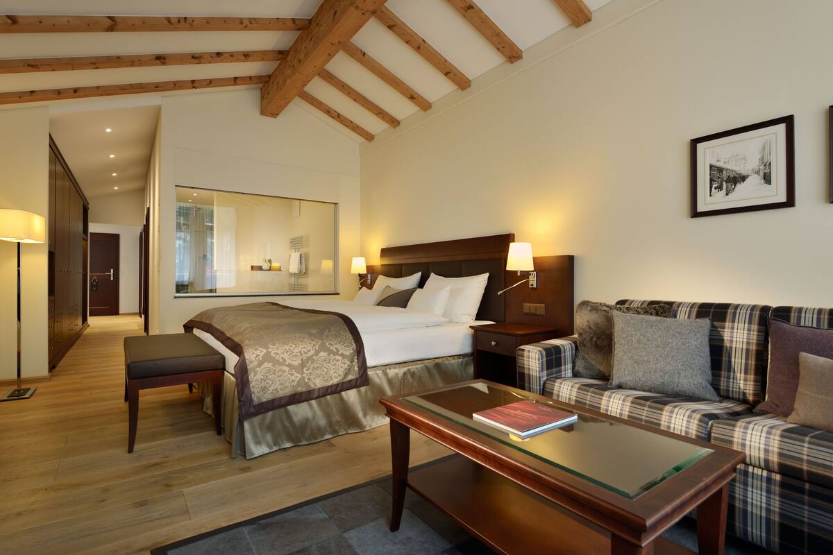 A hotel room with a bed, a sofa, a table, and a mirror.