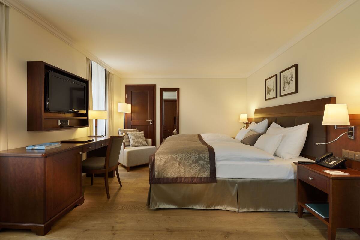 A hotel room with a bed, desk, chair, TV, bedside lamps, and a phone.