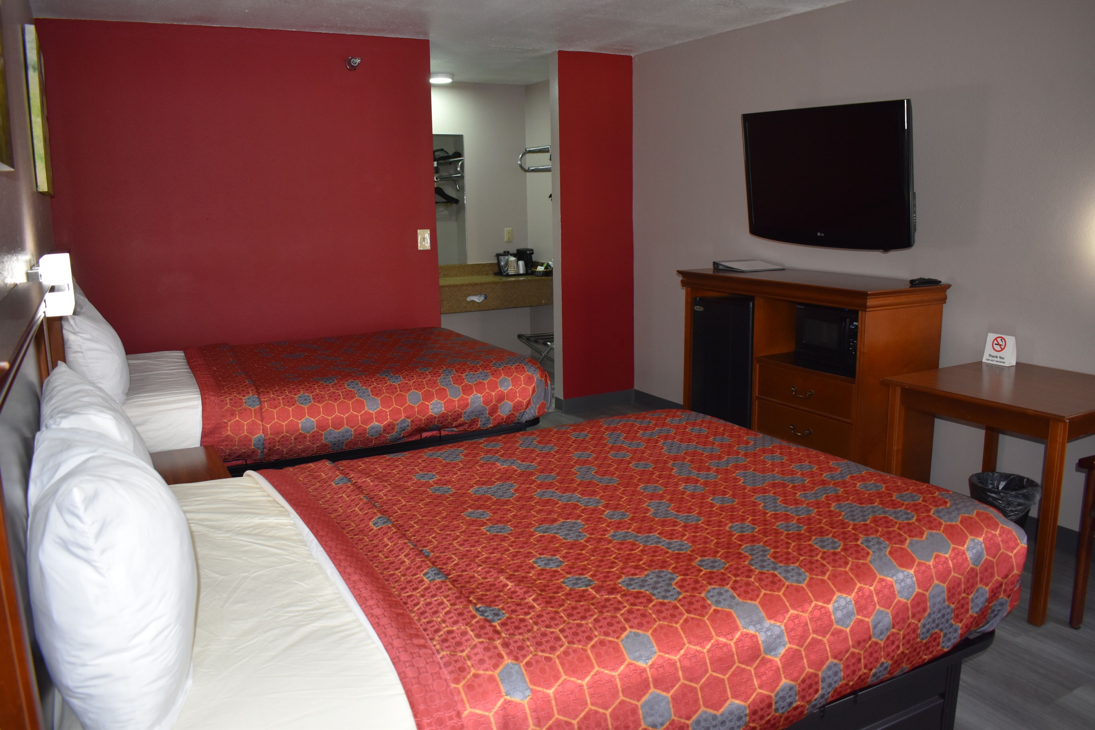 A hotel room with two beds, a TV, a desk, and a mirror.