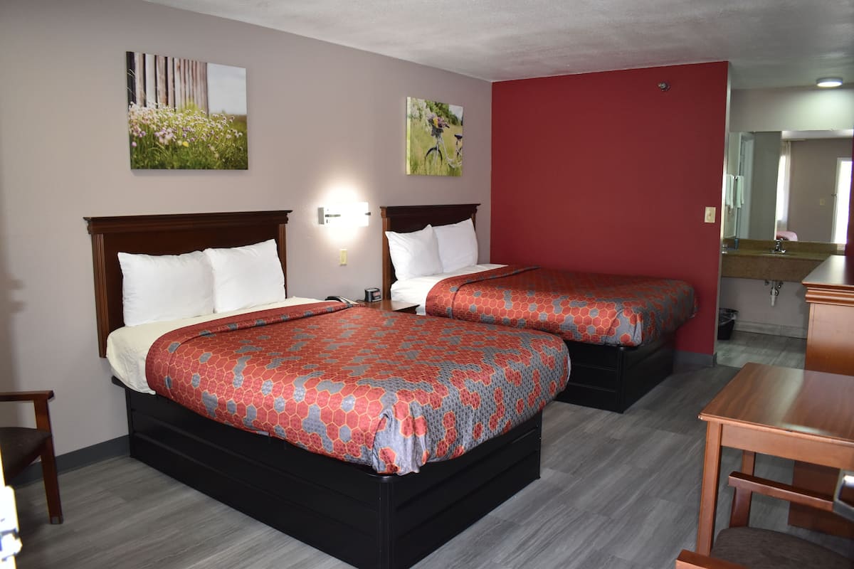 A hotel room with two beds, a wooden headboard, a nightstand, a desk, and a mirror.