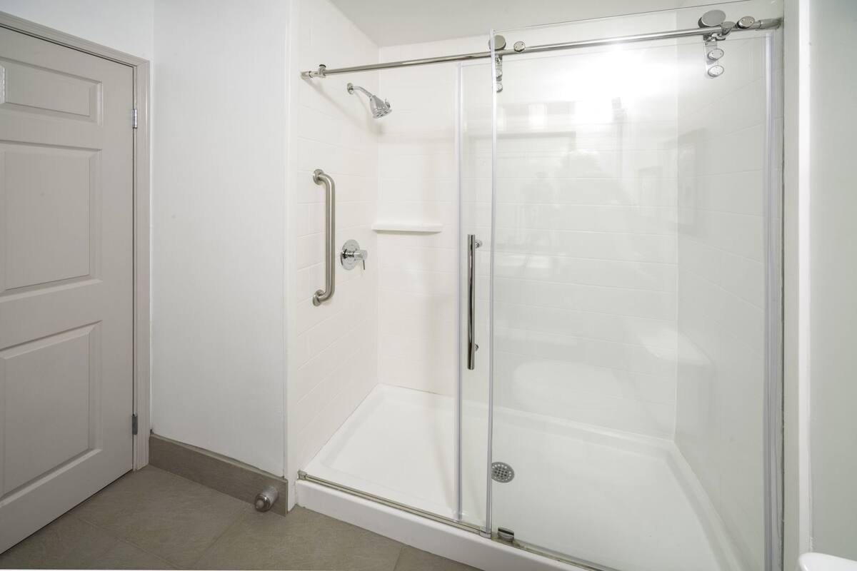 A glass-enclosed shower with a handrail, a door, and a tiled floor.