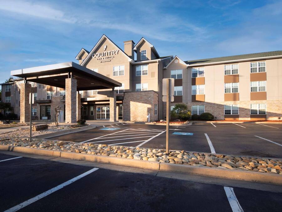 A modern hotel with a covered entrance, a parking lot, and a clear sky.