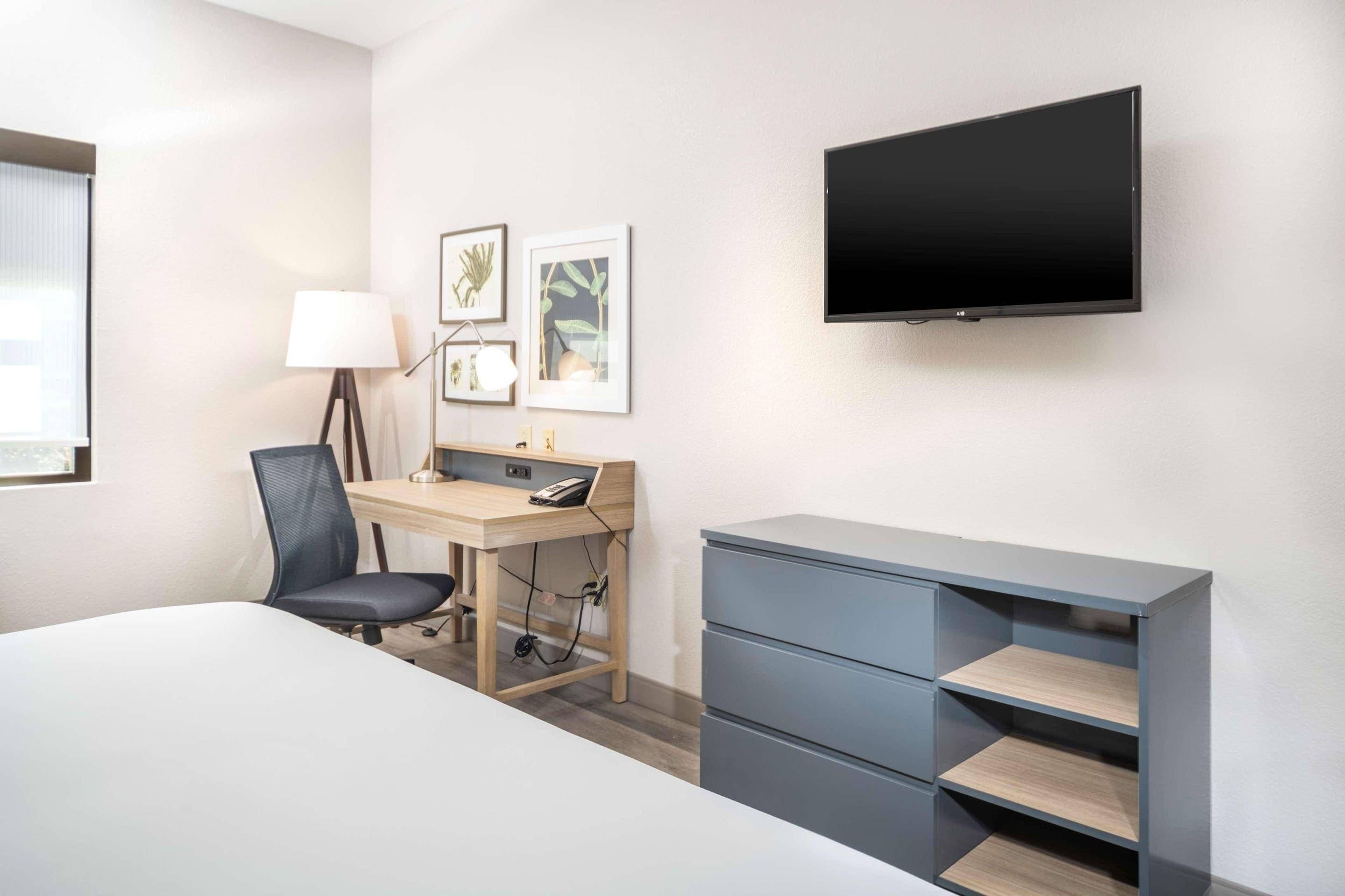 A hotel room with a bed, desk, chair, TV, and storage unit.