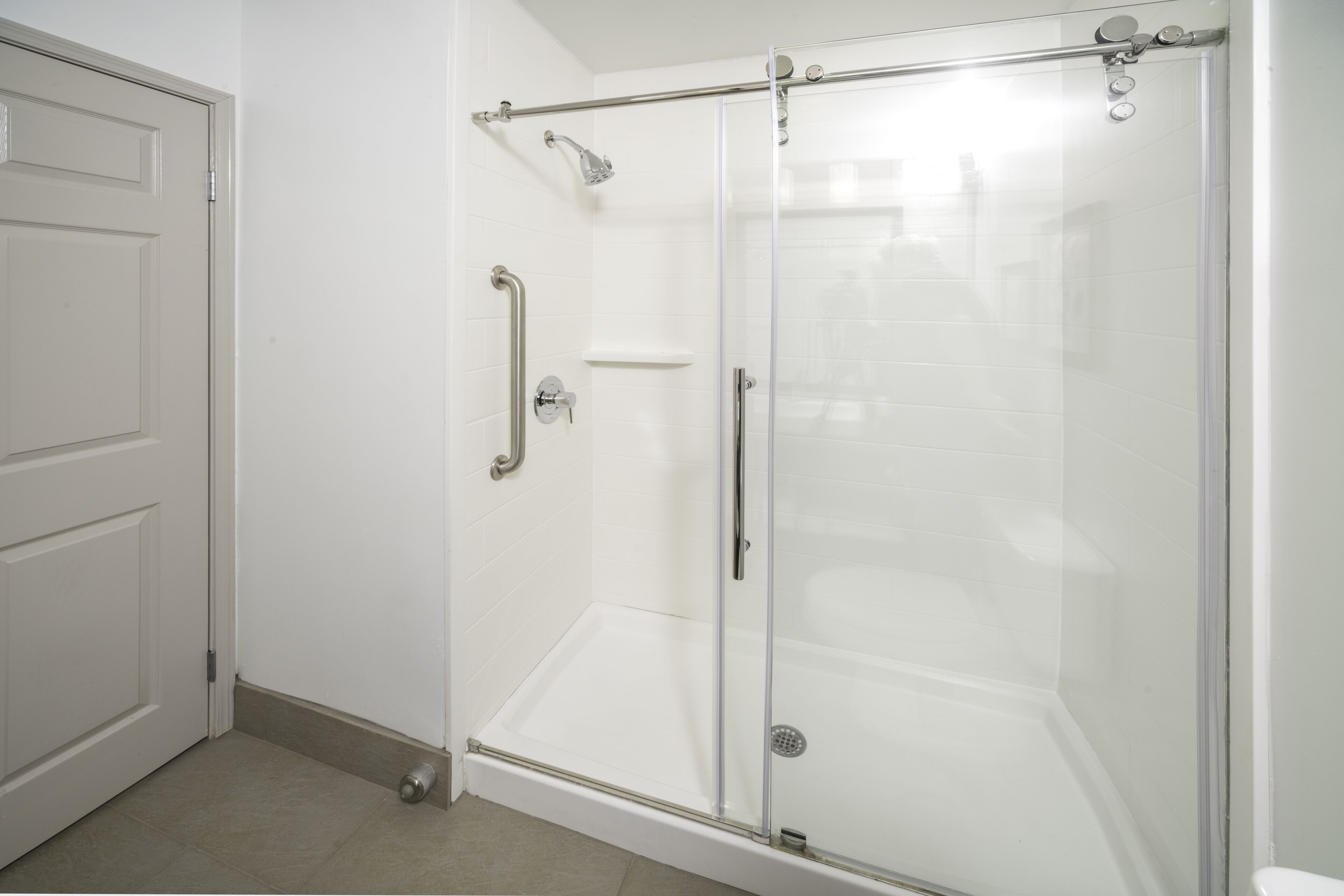 Ducha con mampara de vidrio, cabezal de ducha de mano y control de mano, además de puerta de vidrio.