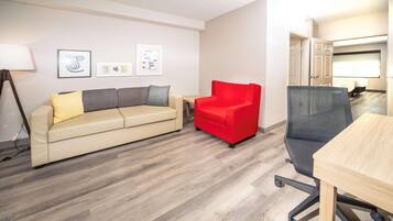 Una sala moderna con un sofá color beige, un sillón rojo y una silla de oficina gris. Hay cuadros enmarcados en la pared, una lámpara de pie y una mesa de madera.
