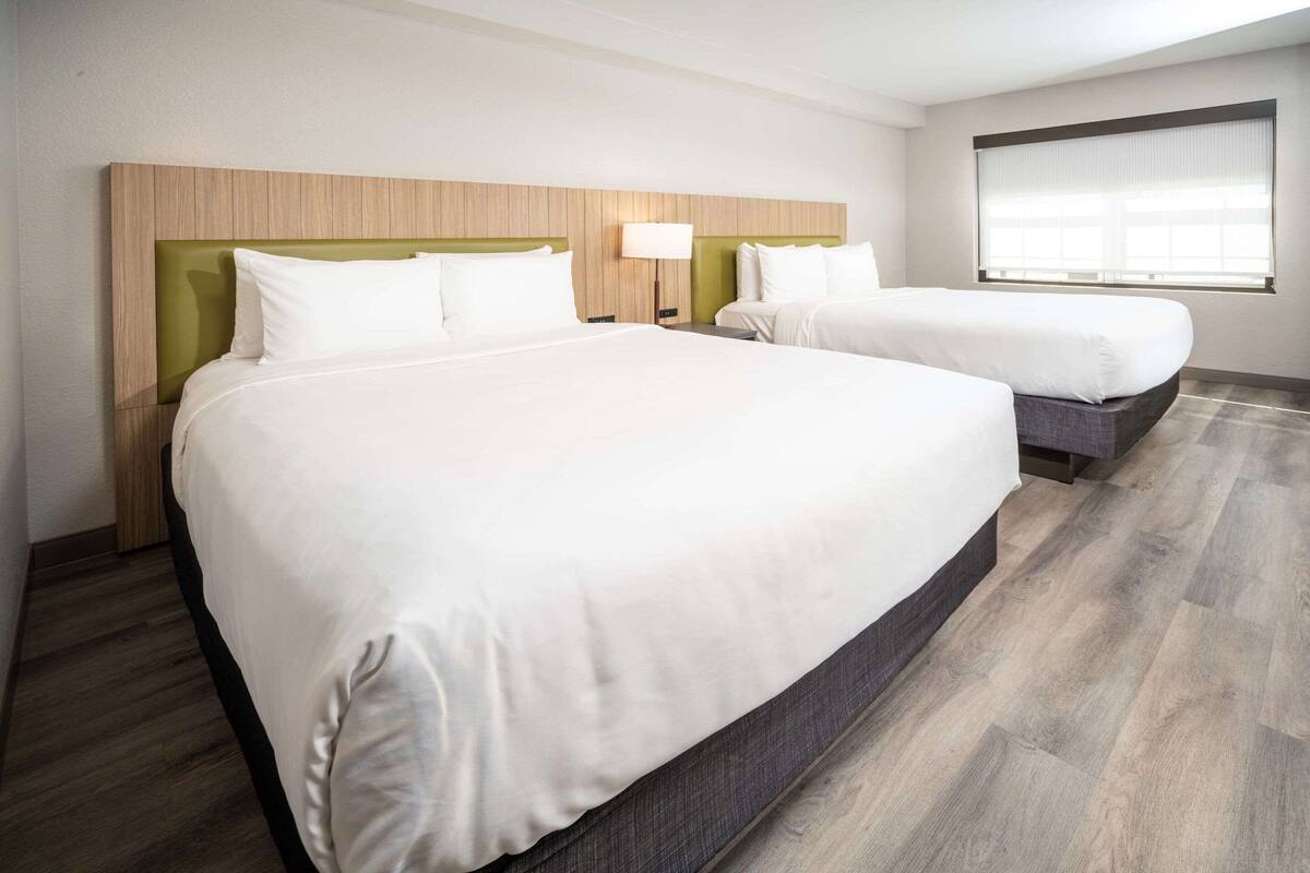 A hotel room with two beds, a wooden headboard, a large window, and a wooden floor.