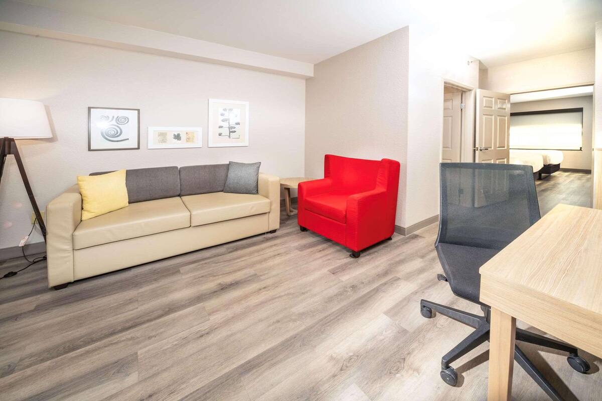 A modern room with a beige sofa, a red chair, a wooden desk, and a black office chair.
