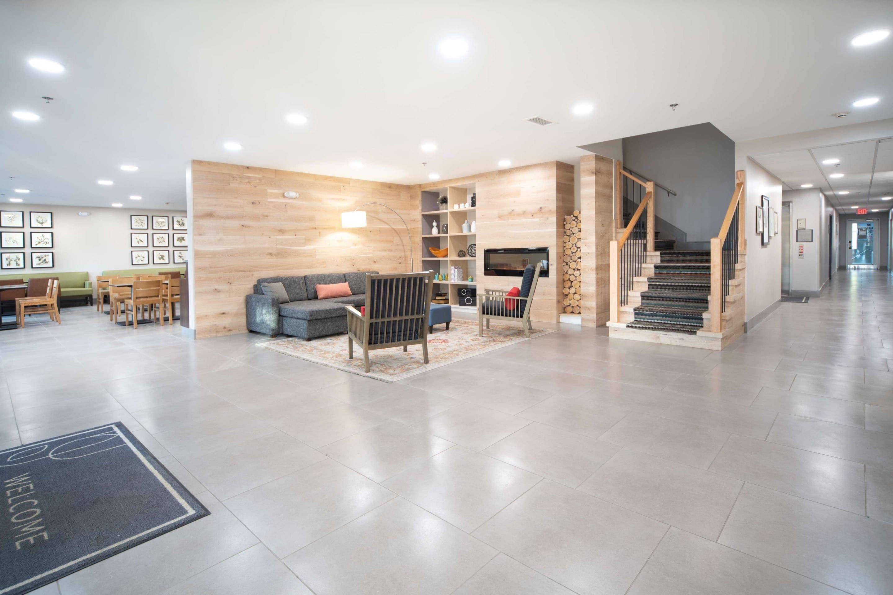 Eine geräumige Lobby mit grauem Sofa, Holzelementen und einer Treppe.