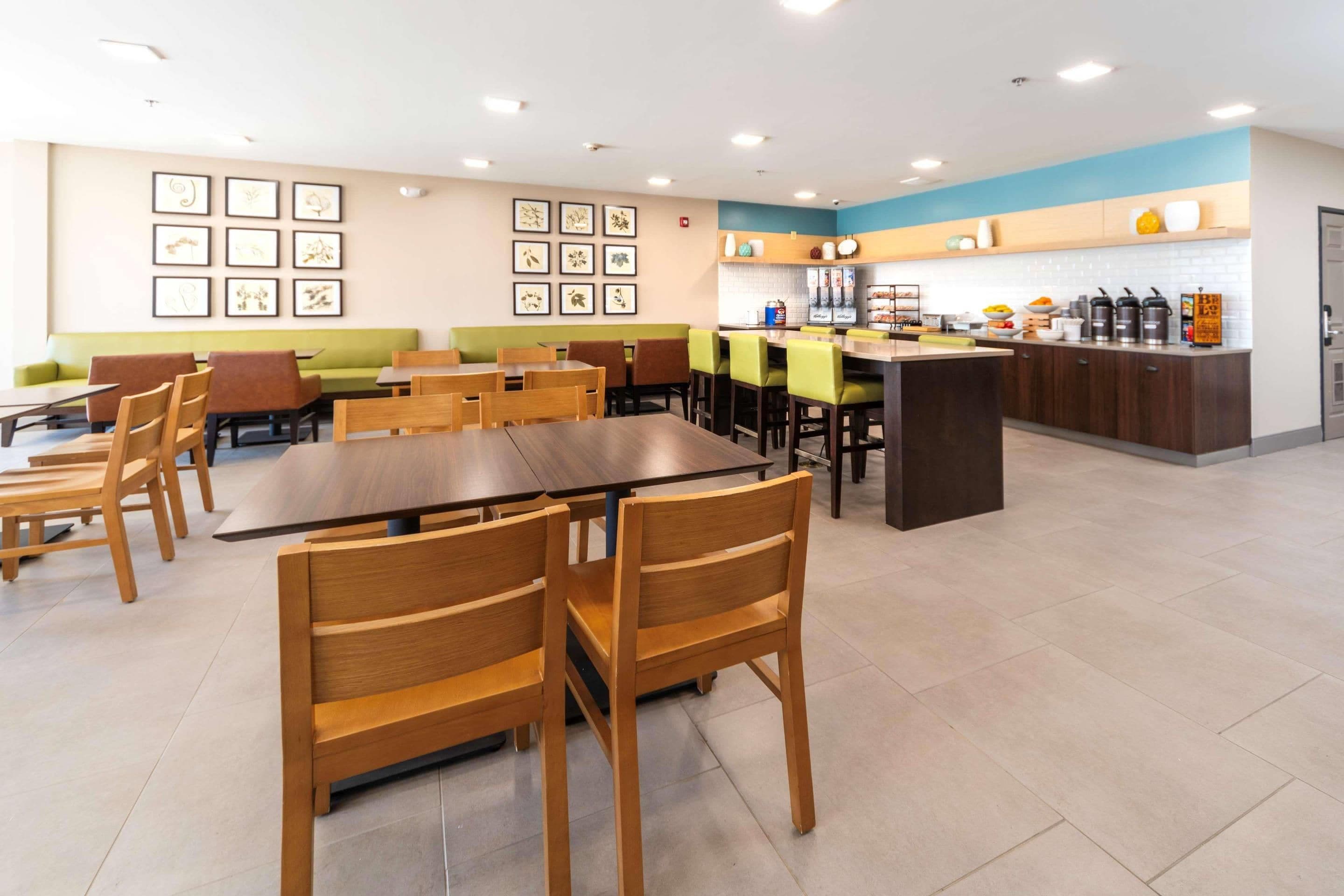 A modern restaurant with wooden tables and chairs, a counter with a beverage station, and framed artwork on the walls.