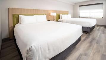 A hotel room with two beds, a wooden headboard, a bedside table with a lamp, and a large window.
