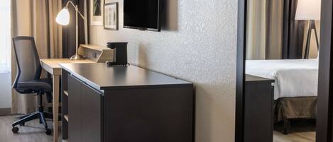 A hotel room with a desk, chair, flat-screen TV, and a bed.