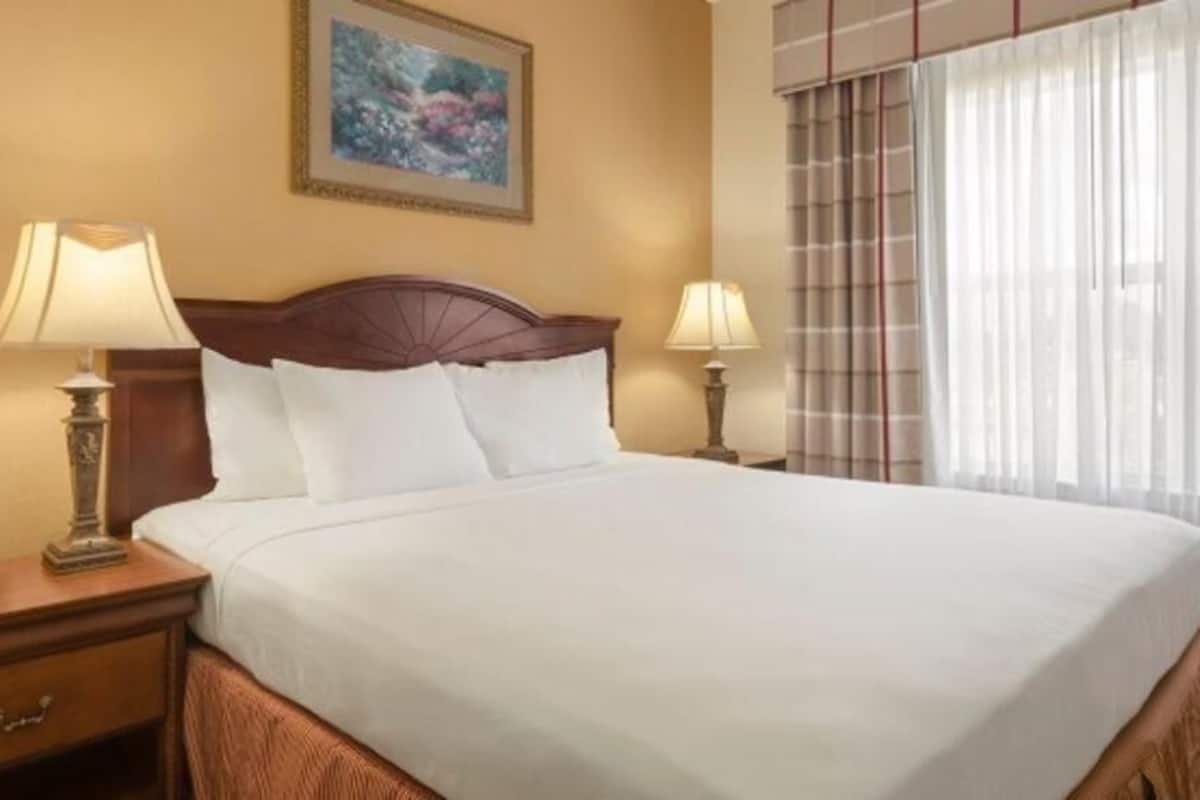 A hotel room with a large bed, two bedside tables with lamps, a painting on the wall, and a window with curtains.