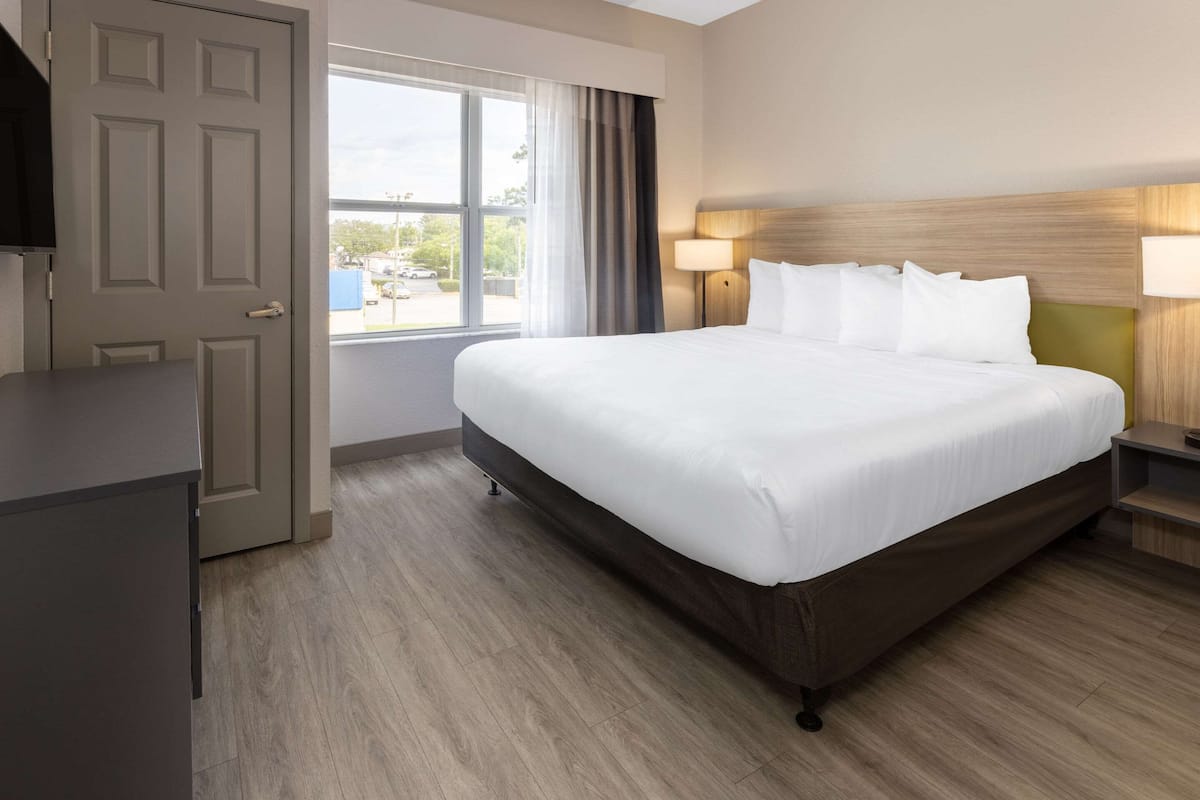 A hotel room with a large bed, a desk, a window with curtains, and a view of the outside.
