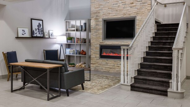 A modern living room with a fireplace, a staircase, and a bookshelf. - Country Inn & Suites by Radisson, Valdosta, GA (Valdosta)