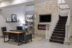 A modern living room with a fireplace, a staircase, and a bookshelf. - Country Inn & Suites by Radisson, Valdosta, GA (Valdosta)