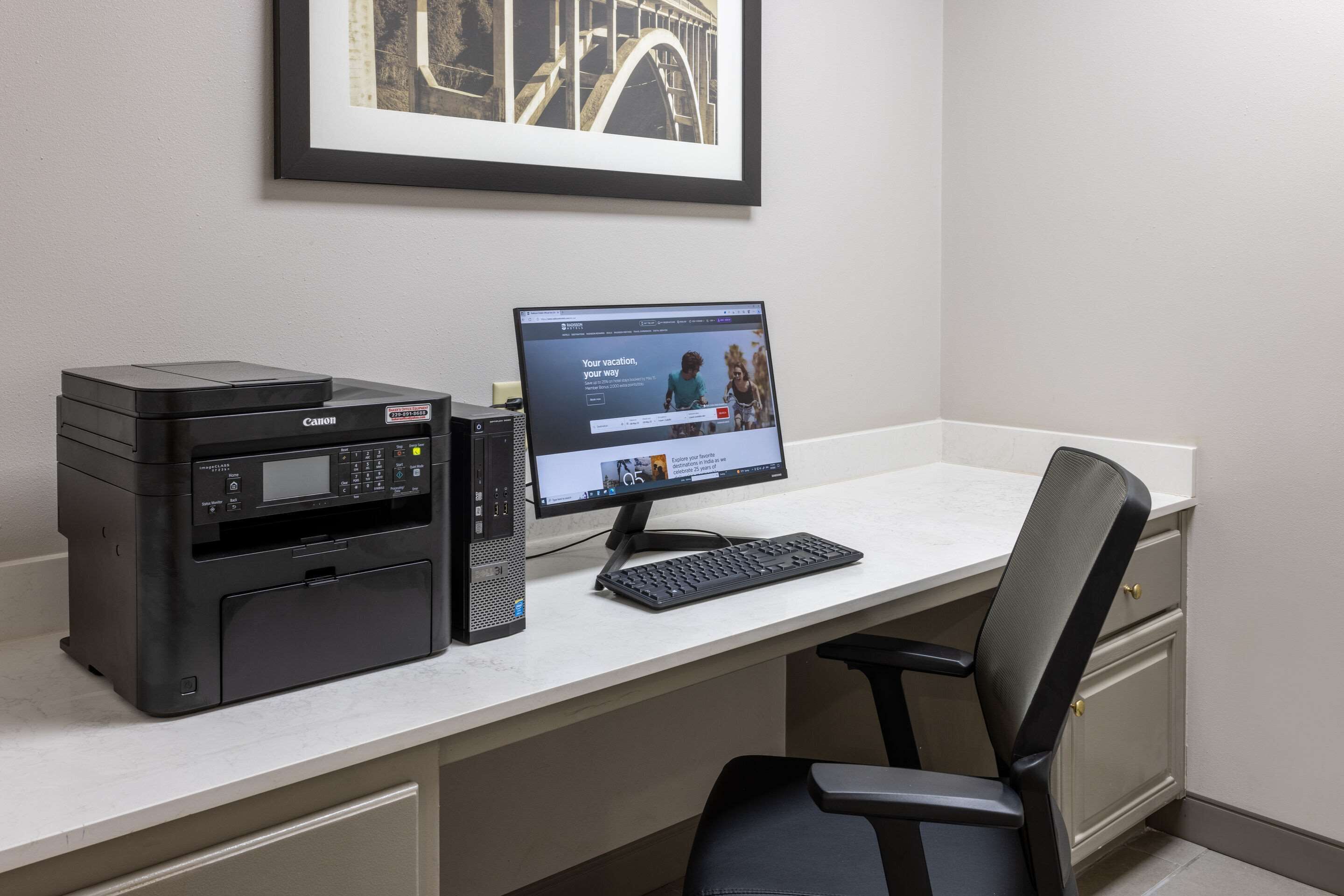 A home office setup with a Canon printer, a desktop computer, and a black office chair.