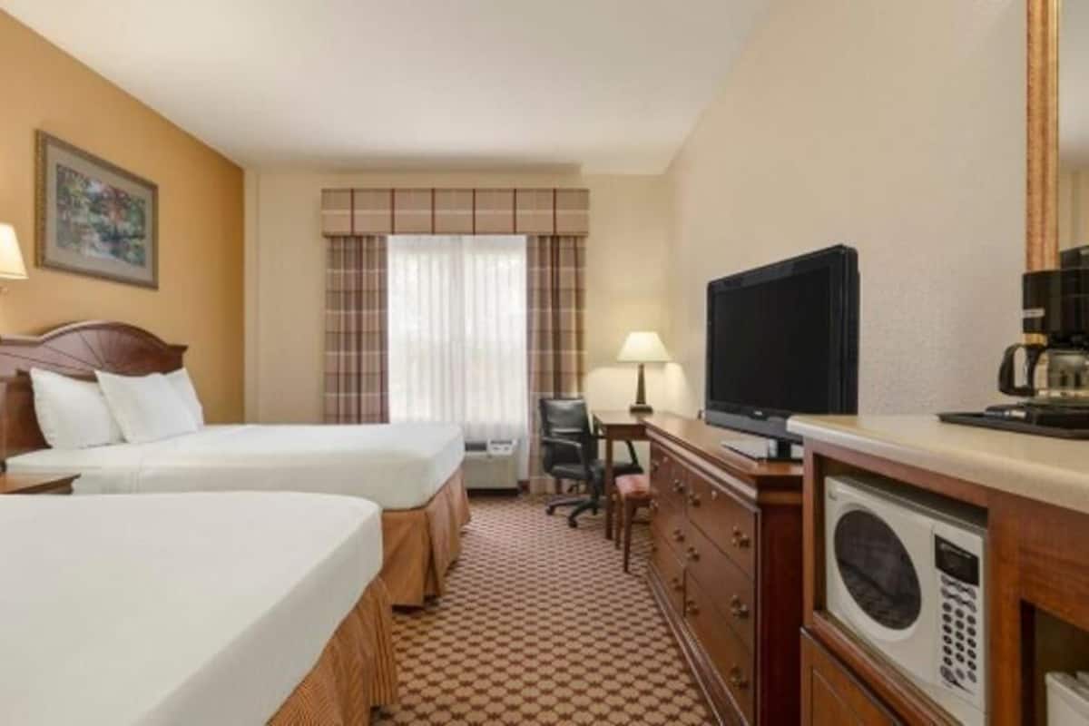 A hotel room with two beds, a television, a coffee maker, a desk with a chair, and a microwave.