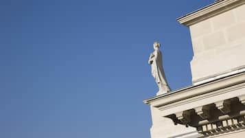 Um edifício com arquitetura clássica, incluindo uma estátua no canto e molduras decorativas.