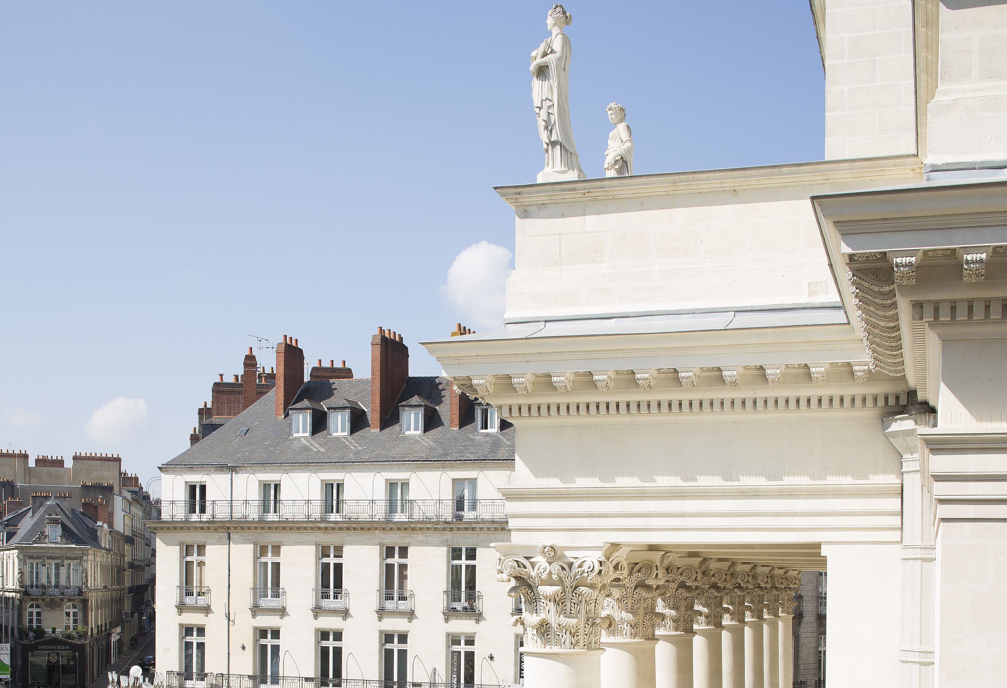 A classical building facade with statues, ornate columns, and a clear blue sky.