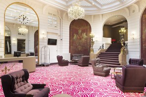 A grand lobby with a patterned carpet, plush seating, a grand staircase, and a large mirror. - Oceania Hôtel de France Nantes (Nantes)