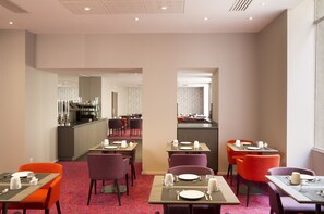 A hotel dining area with tables set for meals, a kitchen in the background, and a patterned carpet. - Oceania Hôtel de France Nantes (Nantes)