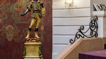 A staircase with a statue on the landing, a candelabra, and a wall with a decorative pattern.