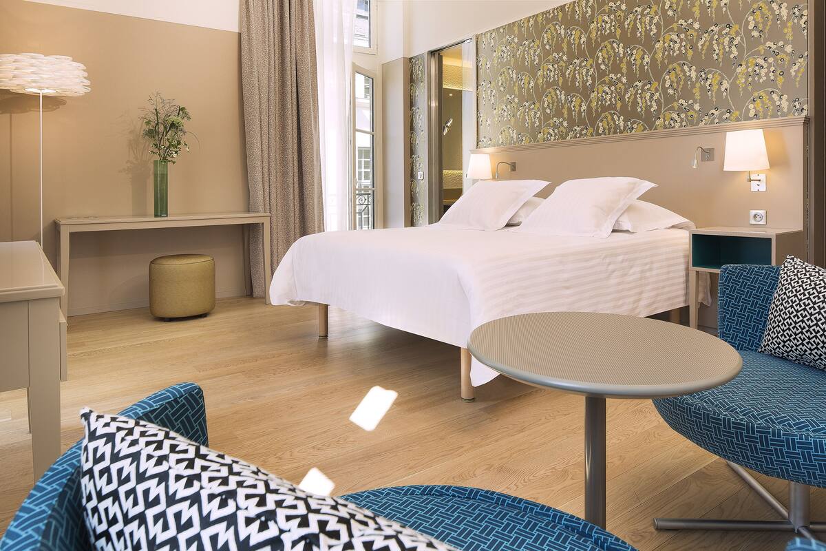 A hotel room with a bed, bedside table, lamp, and a small round table.