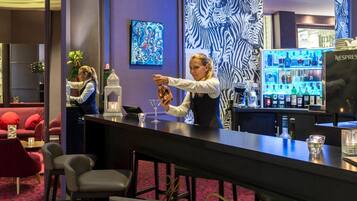 Un coin bar avec un barman, une machine Nespresso et un canapé rouge en arrière-plan.