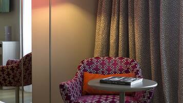 A hotel room with a bed, a chair with a patterned cushion, a small table, and a floor lamp.