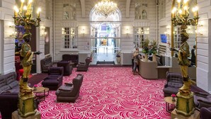 Un lobby espacioso con techo alto, grandes candelabros y una alfombra con diseño.