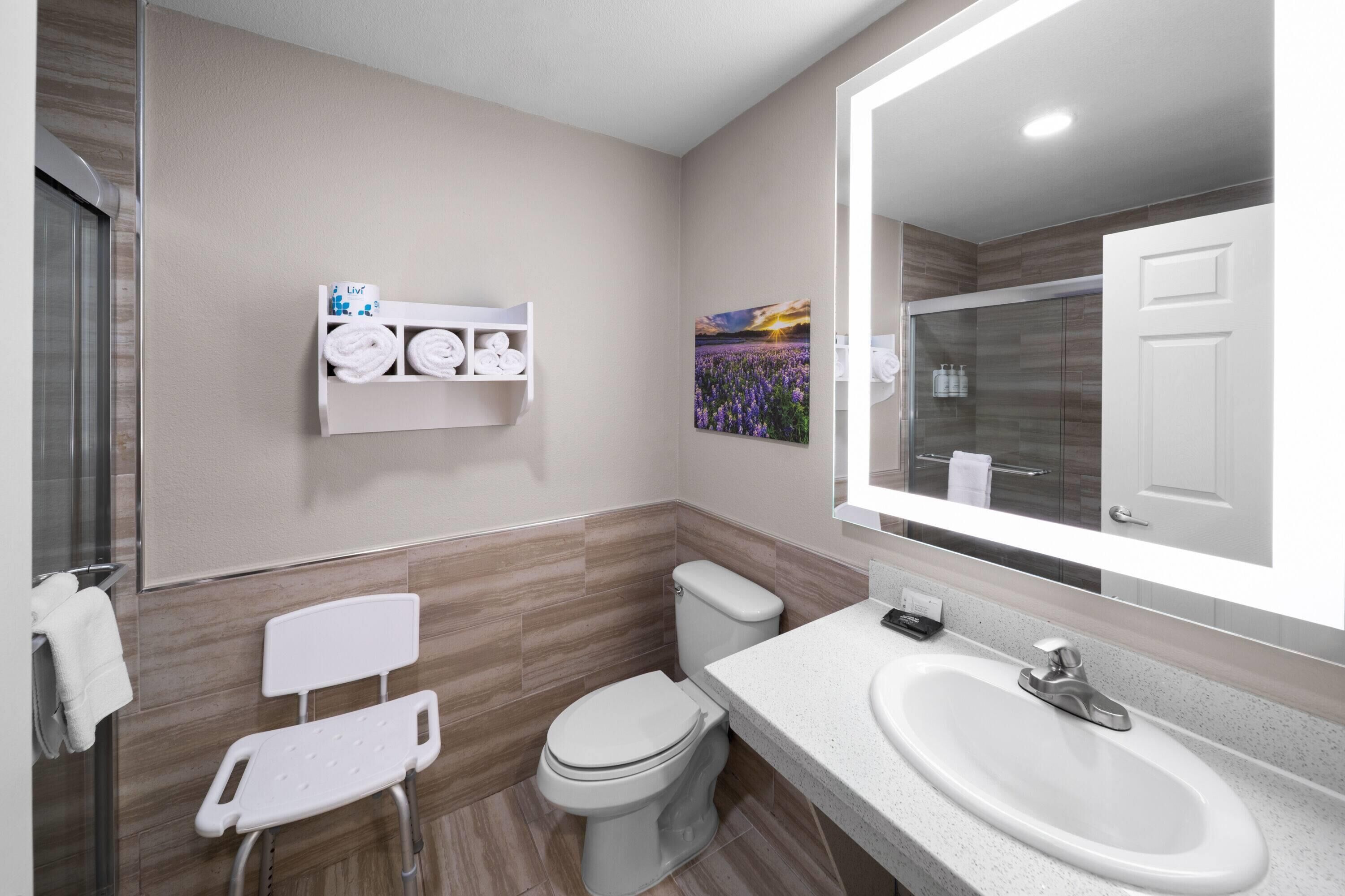 Une salle de bain moderne avec des toilettes, un lavabo, une douche et une chaise blanche.