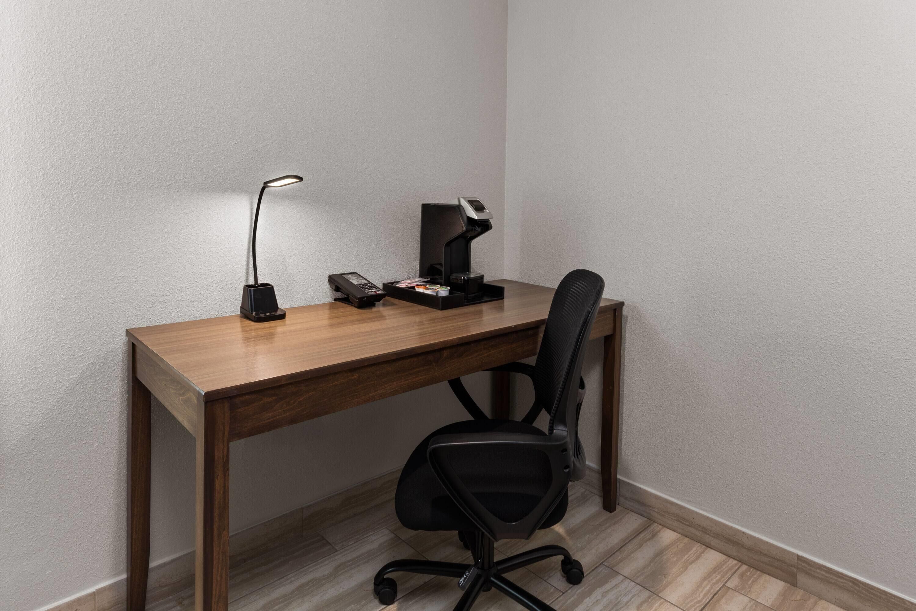 A corner office with a wooden desk, two black office chairs, a desk lamp, a telephone, and a small black object on the desk.